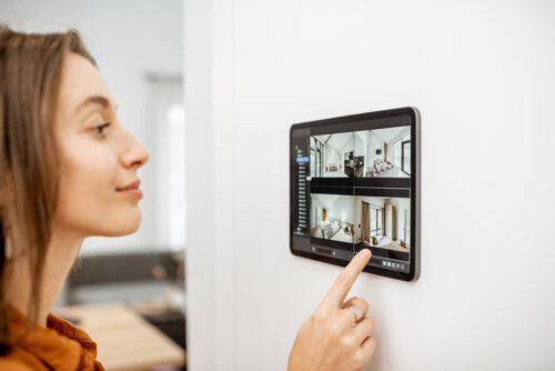 Young woman watching video from security cameras on a digital tablet at home. Concept of remote video surveillance over the internet with smart devices